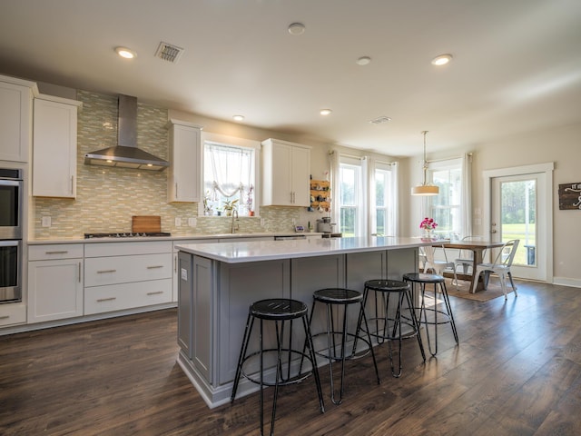 kitchen with wall chimney exhaust hood, decorative light fixtures, a kitchen island, dark hardwood / wood-style flooring, and white cabinetry