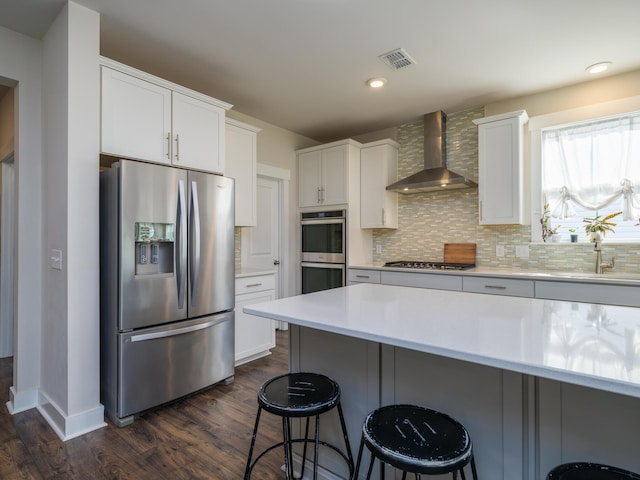 kitchen featuring wall chimney range hood, dark hardwood / wood-style floors, a breakfast bar, white cabinets, and appliances with stainless steel finishes