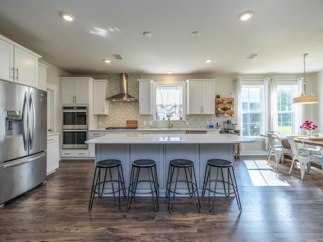 kitchen with white cabinetry, a center island, wall chimney exhaust hood, plenty of natural light, and appliances with stainless steel finishes