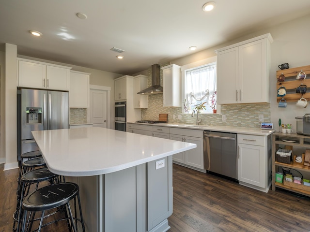 kitchen featuring appliances with stainless steel finishes, dark hardwood / wood-style flooring, wall chimney exhaust hood, white cabinetry, and a kitchen island