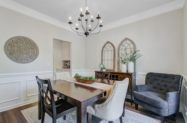 dining space featuring dark wood-style floors, a decorative wall, crown molding, wainscoting, and a notable chandelier