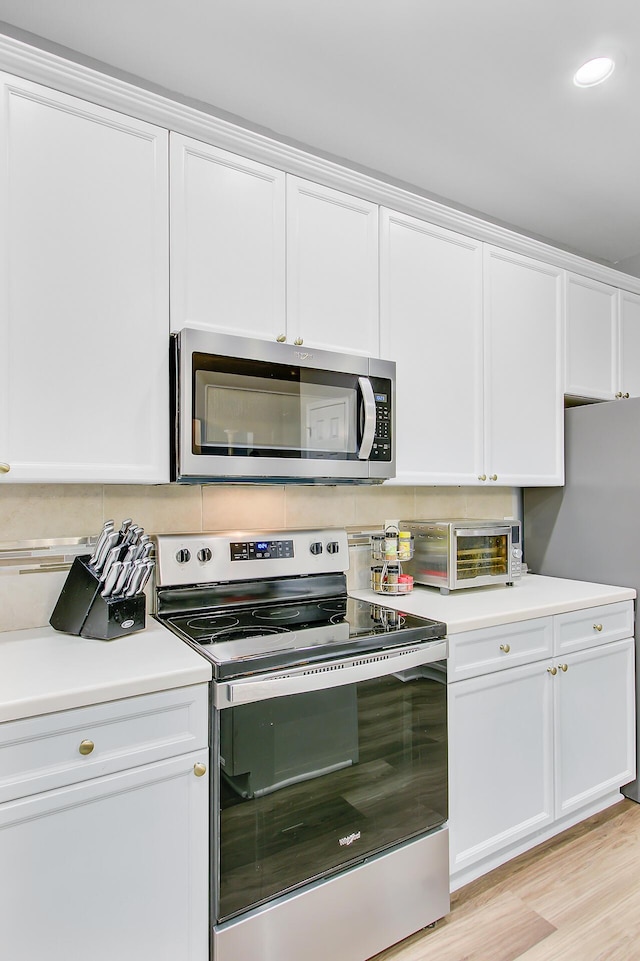 kitchen featuring white cabinets, a toaster, tasteful backsplash, light countertops, and appliances with stainless steel finishes