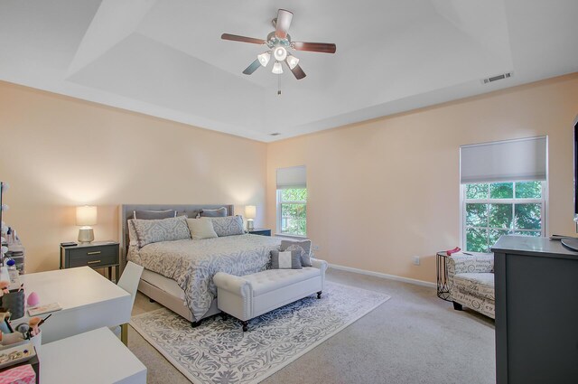 bedroom with a raised ceiling, visible vents, baseboards, light colored carpet, and ceiling fan