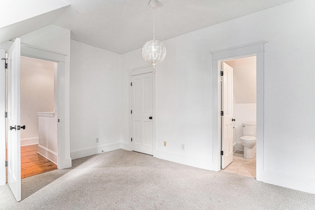 unfurnished bedroom with light colored carpet, lofted ceiling, and connected bathroom