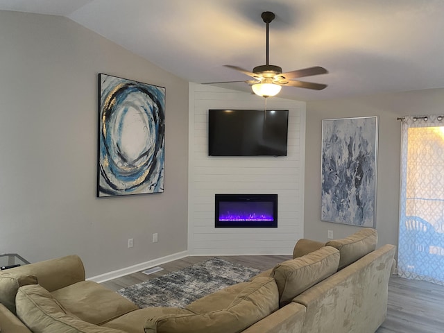 living room with ceiling fan, light wood-type flooring, a fireplace, and vaulted ceiling