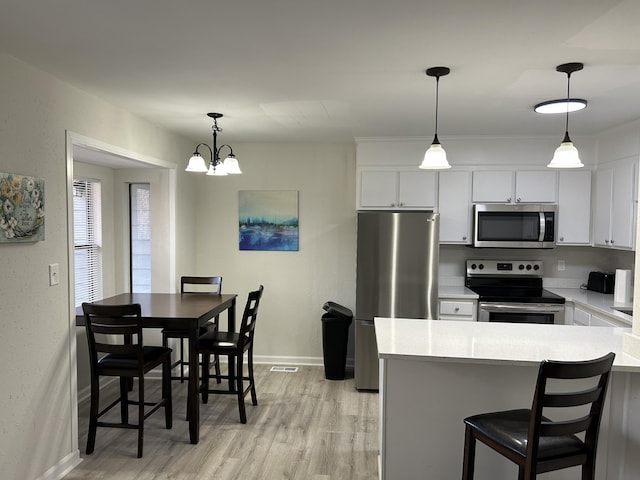 kitchen featuring white cabinetry, hanging light fixtures, stainless steel appliances, a notable chandelier, and a breakfast bar