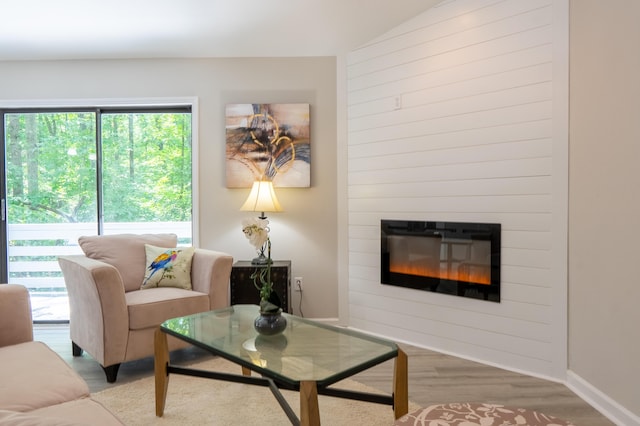 living room with a large fireplace, lofted ceiling, and light hardwood / wood-style flooring