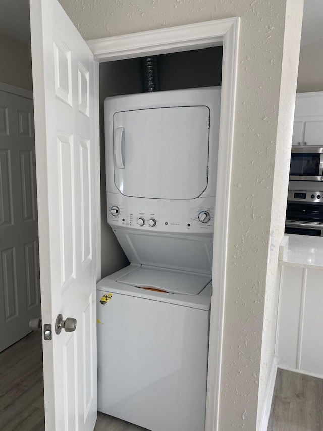 washroom with stacked washer / drying machine and hardwood / wood-style flooring