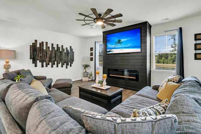 living room featuring ceiling fan, a large fireplace, and wood-type flooring