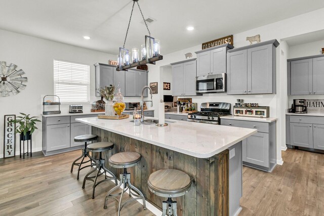 kitchen featuring a center island with sink, stainless steel appliances, light hardwood / wood-style floors, and gray cabinets