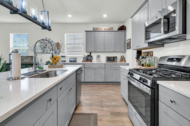 kitchen with light hardwood / wood-style flooring, pendant lighting, gray cabinets, appliances with stainless steel finishes, and sink