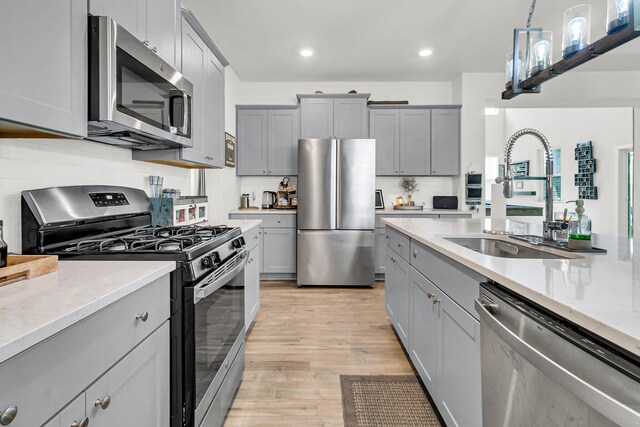 kitchen featuring stainless steel appliances, sink, light wood-type flooring, light stone countertops, and gray cabinets