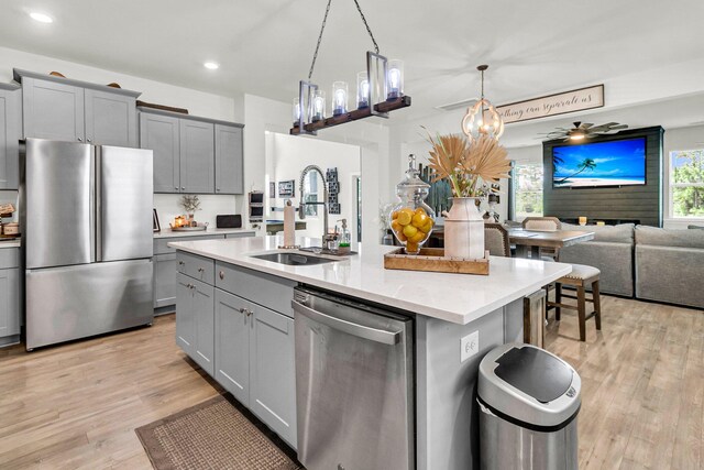 kitchen with stainless steel appliances, light hardwood / wood-style flooring, sink, gray cabinetry, and a kitchen island with sink