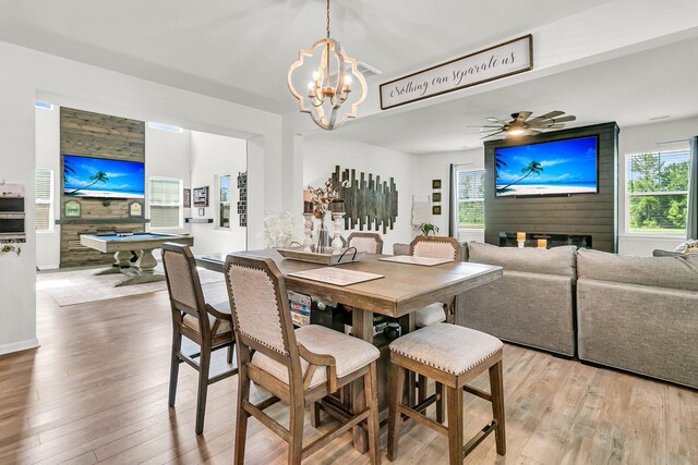 dining space with ceiling fan with notable chandelier, light hardwood / wood-style flooring, wooden walls, and billiards