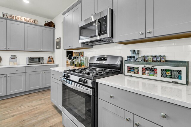 kitchen featuring light hardwood / wood-style floors, stainless steel appliances, gray cabinets, and tasteful backsplash