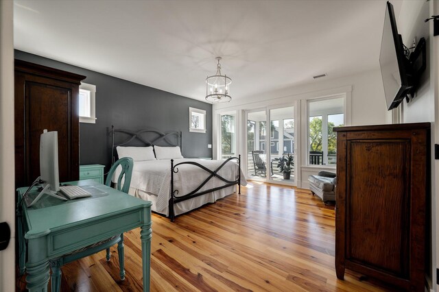 409 W Indian Ave, Folly Beach, SC 29439 - bedroom with light wood-style flooring, access to exterior, a notable chandelier, and multiple windows