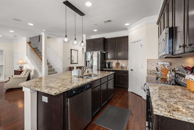 kitchen featuring pendant lighting, sink, appliances with stainless steel finishes, ornamental molding, and an island with sink