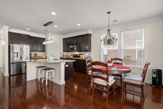 kitchen with decorative light fixtures, dark brown cabinets, stainless steel appliances, a kitchen island with sink, and decorative backsplash