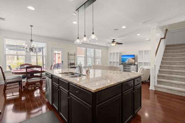 kitchen with sink, hanging light fixtures, dark hardwood / wood-style floors, light stone countertops, and an island with sink