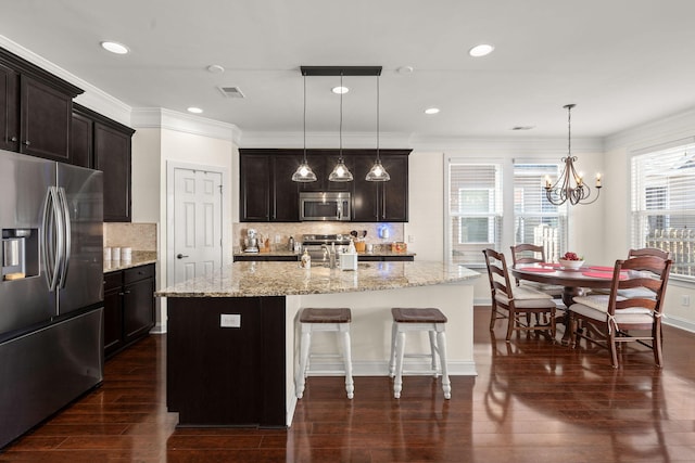 kitchen featuring dark wood-type flooring, stainless steel appliances, decorative light fixtures, and a kitchen island with sink