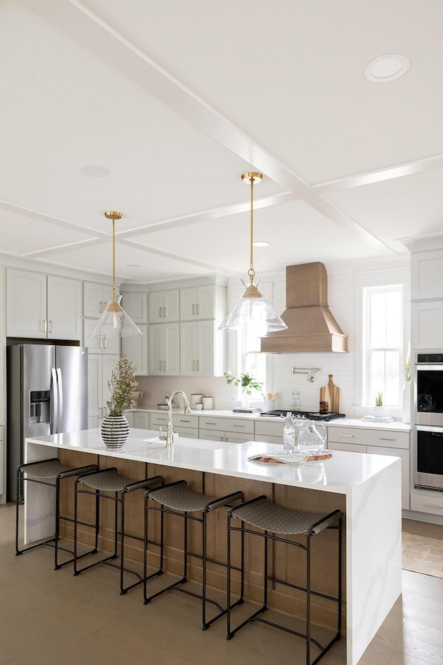 kitchen with a breakfast bar, custom range hood, tasteful backsplash, white cabinetry, and stainless steel appliances