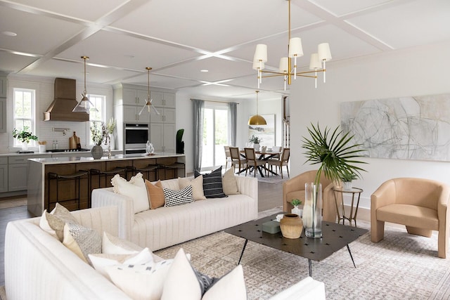 living room featuring an inviting chandelier, coffered ceiling, and light wood-style floors