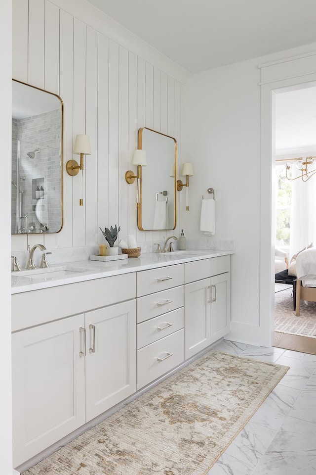 ensuite bathroom with a sink, marble finish floor, a shower stall, and double vanity