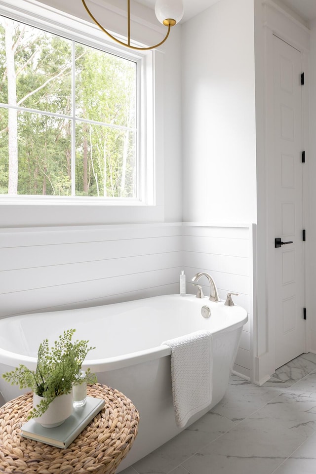 bathroom with marble finish floor and a freestanding bath