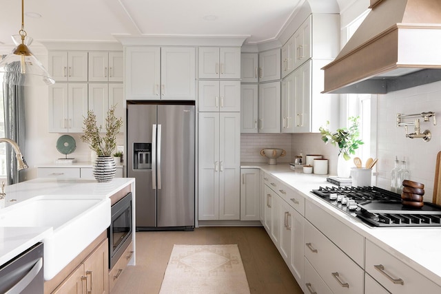 kitchen with custom range hood, a sink, appliances with stainless steel finishes, light countertops, and decorative backsplash