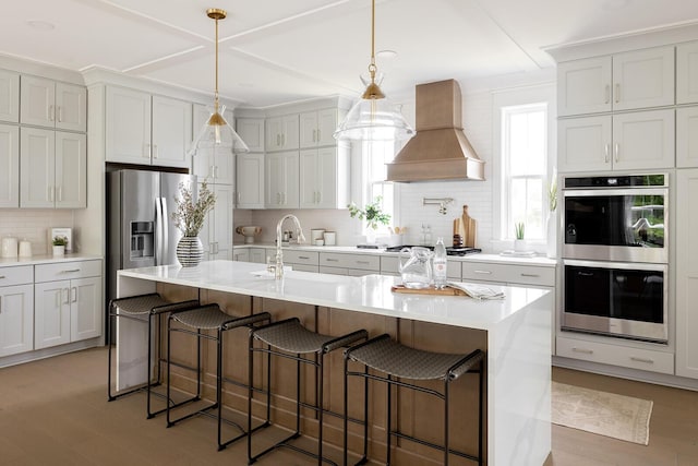 kitchen with backsplash, premium range hood, light countertops, stainless steel appliances, and a sink