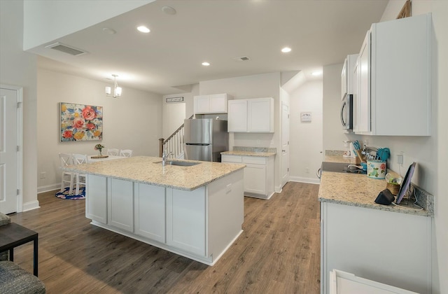 kitchen with light stone countertops, stainless steel appliances, an island with sink, and white cabinets