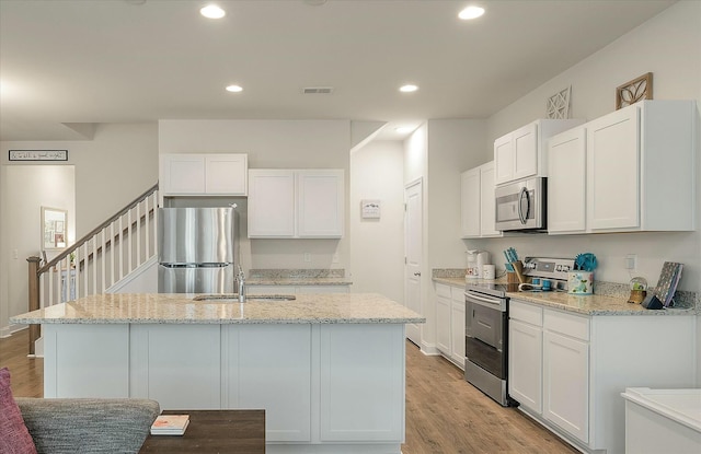 kitchen with stainless steel appliances, white cabinetry, sink, and light hardwood / wood-style floors