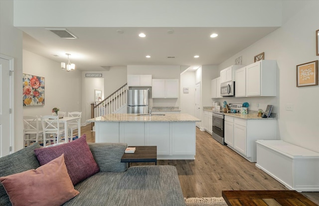 kitchen with light stone countertops, appliances with stainless steel finishes, white cabinets, and light hardwood / wood-style floors