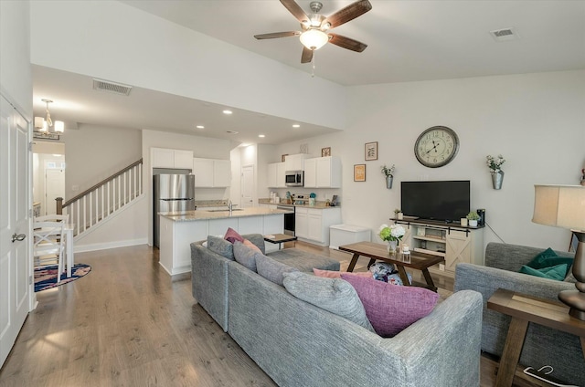 living room with ceiling fan with notable chandelier, sink, vaulted ceiling, and light hardwood / wood-style flooring