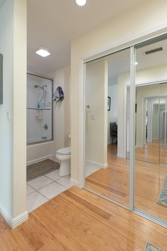 bathroom featuring wood-type flooring, combined bath / shower with glass door, and toilet