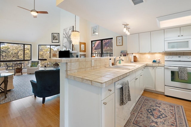 kitchen with white cabinetry, white appliances, kitchen peninsula, and sink