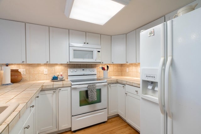 kitchen with tasteful backsplash, white cabinetry, tile counters, and white appliances