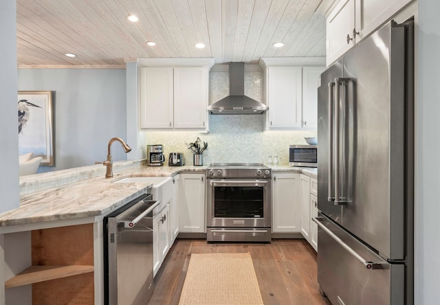 kitchen featuring appliances with stainless steel finishes, white cabinets, kitchen peninsula, wall chimney exhaust hood, and wood-type flooring