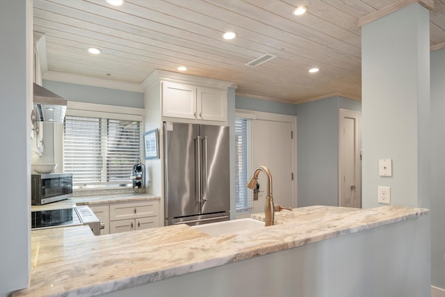 kitchen with light stone countertops, stainless steel appliances, wall chimney exhaust hood, white cabinetry, and wooden ceiling