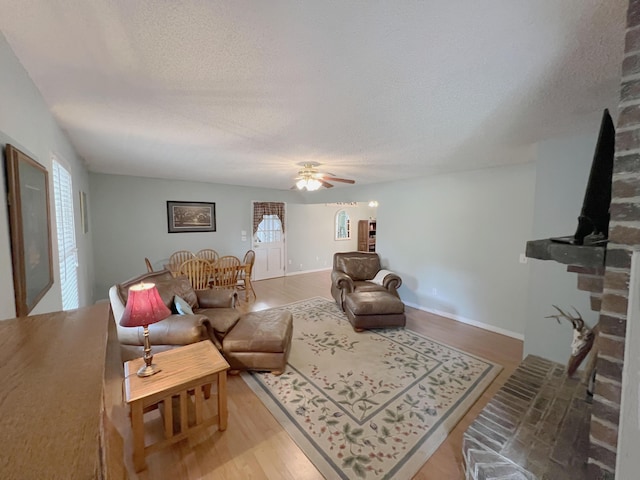 living room with a ceiling fan, a textured ceiling, baseboards, and wood finished floors