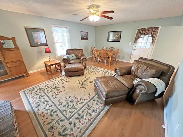 living area featuring baseboards, a textured ceiling, wood finished floors, and a ceiling fan