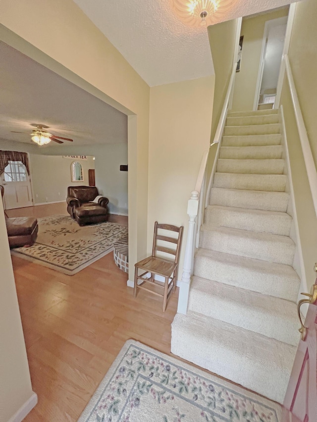 staircase featuring a ceiling fan, a textured ceiling, and wood finished floors