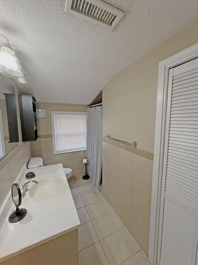 full bathroom with tile patterned flooring, a textured ceiling, tile walls, and visible vents