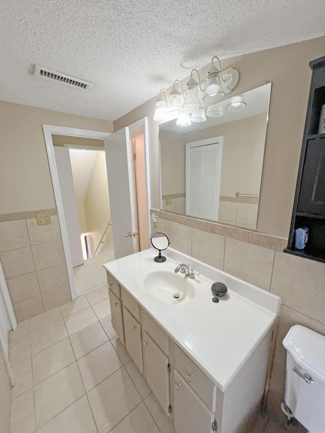 bathroom featuring vanity, tile walls, toilet, a textured ceiling, and visible vents
