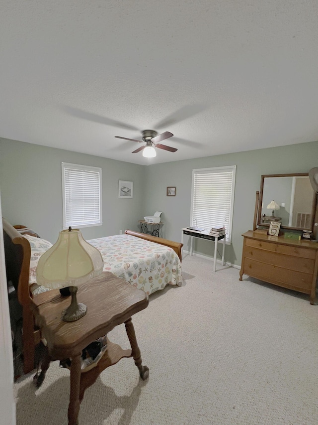 bedroom with light colored carpet, ceiling fan, baseboards, and a textured ceiling