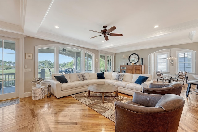 living area featuring arched walkways, a raised ceiling, ornamental molding, and ceiling fan with notable chandelier