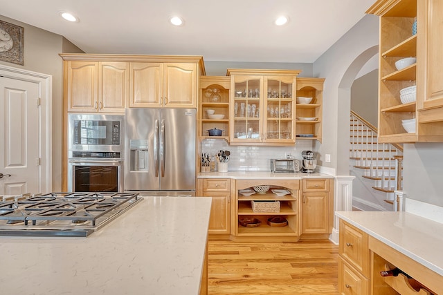 kitchen with light brown cabinets, arched walkways, appliances with stainless steel finishes, and open shelves