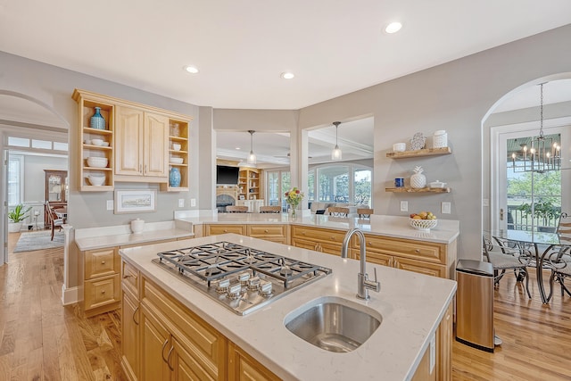 kitchen featuring light brown cabinets, open shelves, a sink, stainless steel gas stovetop, and arched walkways