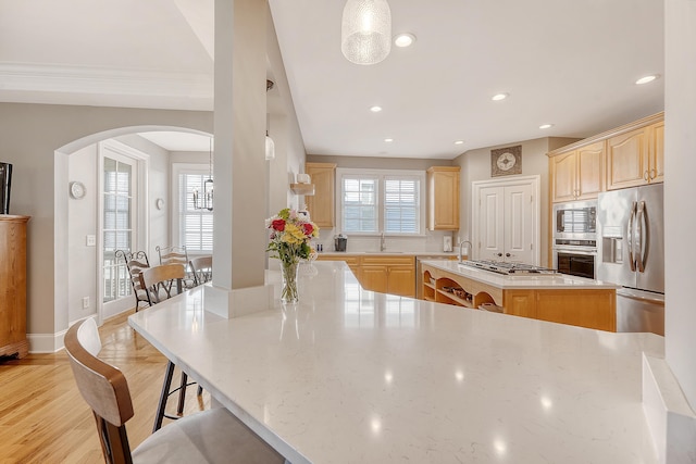 kitchen with a kitchen breakfast bar, stainless steel appliances, light brown cabinets, arched walkways, and a kitchen island with sink