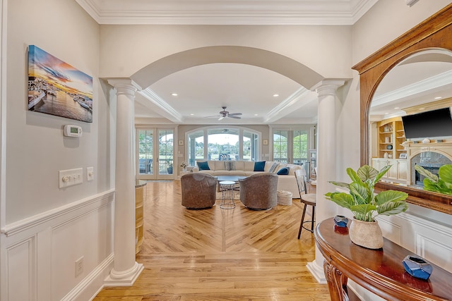 interior space with decorative columns, arched walkways, a ceiling fan, and crown molding
